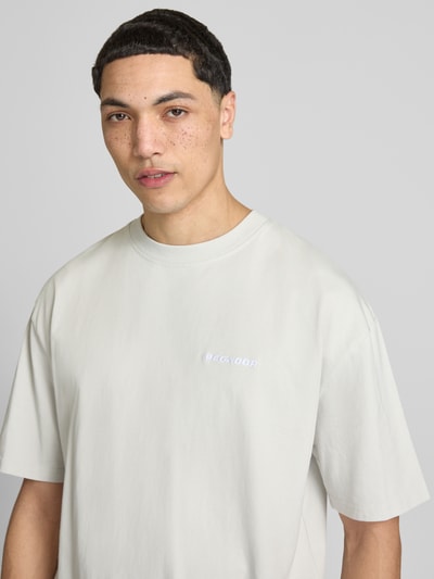 Mannenmodel draagt Oversized T-Shirt met Logo-Stitching van Pegador, pure katoen, oversized fit, ronde hals, lichtgrijs met logo, close-up bovenlichaam.