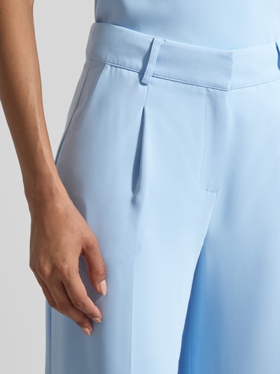 Frauenmodel trägt Wide Fit Stoffhose mit Bügelfalten von Christian Berg Cocktail in Hellblau, glatte Textur, Gesäßtaschen, Nahaufnahme Oberkörper.