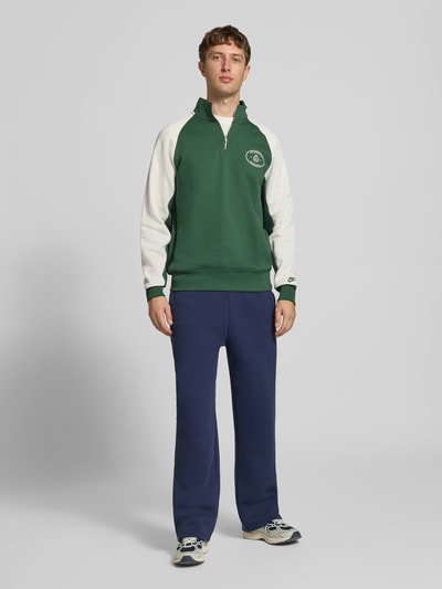 Männermodel trägt Relaxed Fit Sweatshirt aus Baumwoll-Mix von Nike in Grün und Weiß, kombiniert mit blauen Hosen, Ganzkörperansicht von vorne. Herren Sweatshirt von Nike.