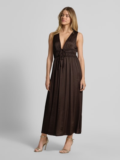 Frauenmodel trägt Maxikleid mit tiefem V-Ausschnitt Modell 'Marja' von mbyM im Material-Mix mit Viskose-Anteil, taillierter Schnitt, Schnürung, glänzende braune Oberfläche, Ganzkörperansicht von vorne.