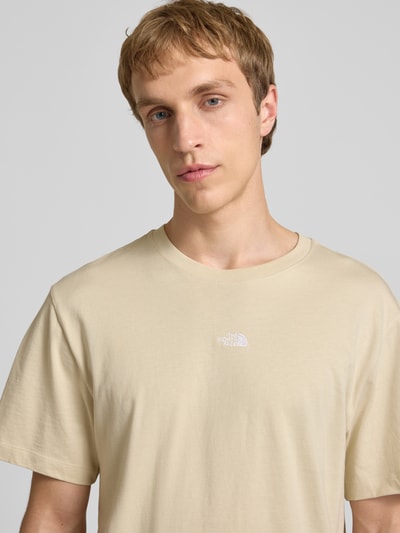 Männermodel trägt T-shirt mit logo-stitching van The North Face in beige, puur katoen, recht model, ronde hals, nahaufnahme bovenlichaam.