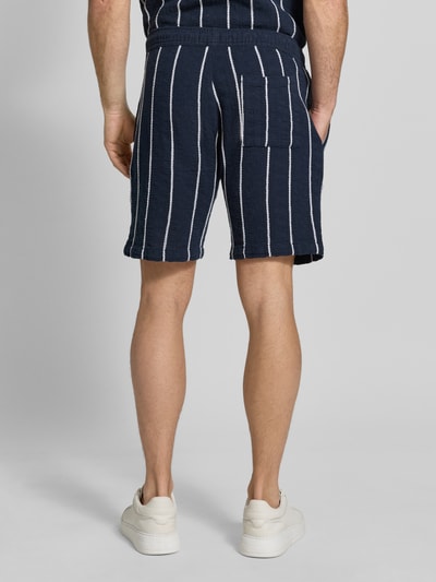 Mężczyzna nosi Shorts mit elastischem Bund und Tunnelzug od MCNEAL, granatowy kolor, białe pionowe paski, krój regular fit, czysta bawełna, elastyczny pas, tunel, Szerokość w rozmiarze M: 42 cm, długość nogawki od wewnątrz: 20 cm, tekstura miękka, widok całej sylwetki z tyłu