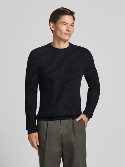 Männermodel trägt Strickpullover aus Kaschmir mit Rundhalsausschnitt von FTC Cashmere, grob gestrickt, in dunklem Farbton, Ganzkörperansicht von vorne.