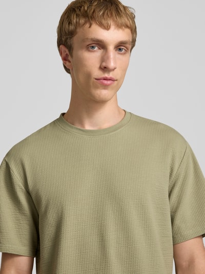 Männermodel trägt Regular Fit T-Shirt aus Baumwoll-Mix Modell 'KIAN' von Only & Sons in Optik: Unifarben mit Rundhals, Ärmelform: Kurzarm, Materialverarbeitung: Piqué, Nahaufnahme Oberkörper.