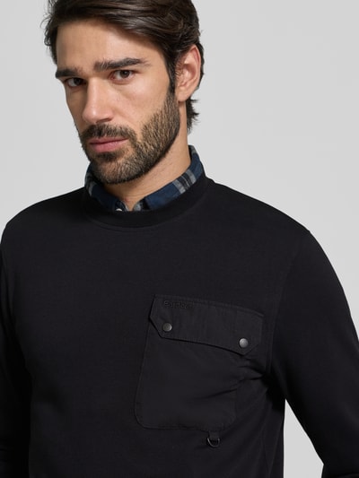 Männermodel trägt Relaxed Fit Langarmshirt aus Baumwoll-Mix von Barbour, Optik: unifarben, Label-Schriftzug, Metall-Akzente, Brusttasche, Rundhals, Nahaufnahme Oberkörper.