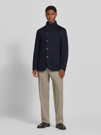 Männermodel trägt Regular Fit Jacke aus Modal-Baumwoll-Mix mit Woll-Anteil von Emporio Armani in Dunkelblau, Stehkragen, aufgesetzte Taschen, asymmetrische Knopfleiste, Ganzkörperansicht von vorne.