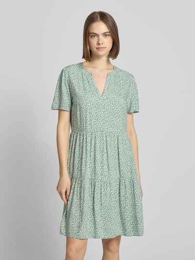 Frauenmodel trägt Tailliertes Sommerkleid aus reiner Viskose Modell 'ZALLY LIFE' von Only, Optik: Allover-Muster, Mini-Länge, V-Ausschnitt, Ärmelform: Kurzarm, Material: Viskose, sanfte Grüntöne mit weißem Muster, glatte Textur, Ganzkörperansicht von vorne.