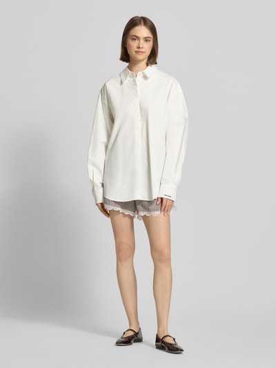 Frauenmodel trägt Oversized Hemdbluse mit Statement-Stitching Modell 'Leya' von OH APRIL aus Reine Baumwolle, Oversized-Fit, verdeckte Knopfleiste, Hemdblusenkragen, abgerundeter Saum, Farbe weiß, glatte Textur, Ganzkörperansicht von vorne.