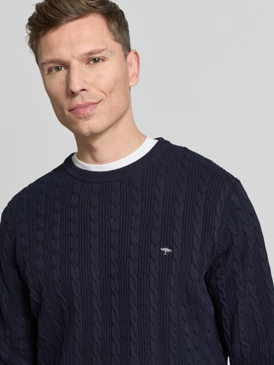 Männermodel trägt Strickpullover mit Zopfmuster und Label-Stitching von Fynch-Hatton, Reine Baumwolle, Slim-Fit, Rundhalsausschnitt, Nahaufnahme Oberkörper.