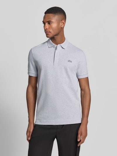 Männermodel trägt Regular Fit Poloshirt aus bawełny-mix von Lacoste, jednokolorowy, wyhaftowane logo, pika, krótki rękaw, kołnierzyk polo, widok z przodu, ujęcie całej sylwetki.