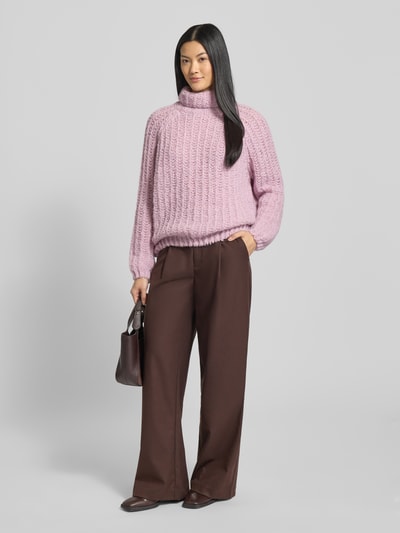 Frauenmodel trägt Strickpullover mit Rollkragen von Smith and Soul in Helllila, lockerer Schnitt, gerippte Abschlüsse, Materialmix mit Alpaka, kombiniert mit weiter brauner Hose, Ganzkörperansicht von vorne.