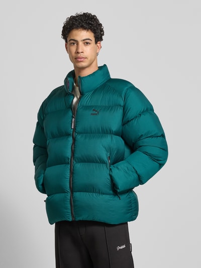 Männermodel trägt Steppjacke mit Label-Print von PUMA PERFORMANCE in Dunkelgrün, gerader Schnitt, Stehkragen, Reißverschlusstaschen, Ganzkörperansicht von vorne.