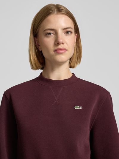 Kobiece model prezentuje Relaxed Fit Sweatshirt aus Baumwoll-Mix od Lacoste, bordowy kolor, miękka faktura, damska bluza, zbliżenie na górną część ciała