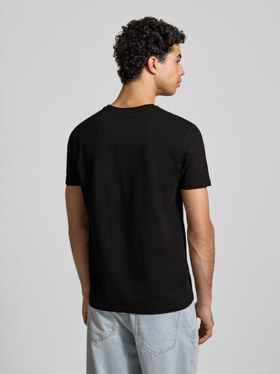 Męski model nosi T-Shirt mit Label-Print od Alpha Industries w kolorze czarnym, prosty krój, bawełna, widok całej sylwetki z tyłu.