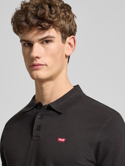 Männermodel trägt Poloshirt mit Label-Detail von Levi's®, Reine Baumwolle, Regular Fit, schwarze Farbe, Nahaufnahme Oberkörper.