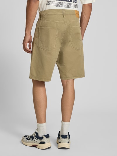 Męski model nosi bermudy z bawełny, 5 kieszeni, krój straight fit, model 'TONY ORIGINAL' od Jack & Jones, kolor beżowy, długość wewnętrzna nogawki 20 cm, szerokość w rozmiarze M 42 cm, zapięcie na guzik i zamek błyskawiczny, widok całej sylwetki z tyłu.