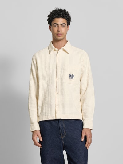 Männermodel trägt Regular Fit Freizeithemd mit Logo-Stitching von REVIEW aus cremefarbener Baumwolle mit Strukturmuster, Ganzkörperansicht von vorne.