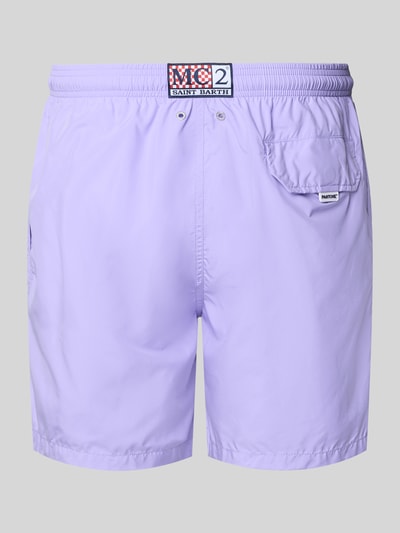 Männermodel trägt Badehose mit Logo-Print Modell 'Lighting Pantone' von MC2 Saint Barth in Lila mit Logo-Patch, Ganzkörperansicht Rückansicht.