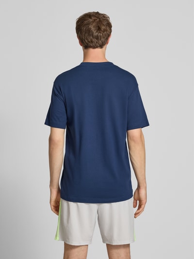 Männermodel trägt Herren T-Shirt mit Logo und Rundhalsausschnitt von New Balance in Dunkelblau, Reine Baumwolle, Regular-Fit, Rückenlänge 74 cm, Ganzkörperansicht Rückansicht.