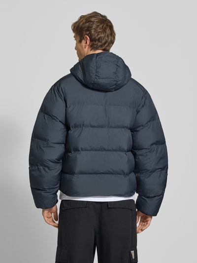 Männermodel trägt Regular Fit Puffer Jacket mit Kapuze von adidas Originals in einfarbigem Dunkelblau, wasserabweisende Webware, Ganzkörperansicht Rückansicht.