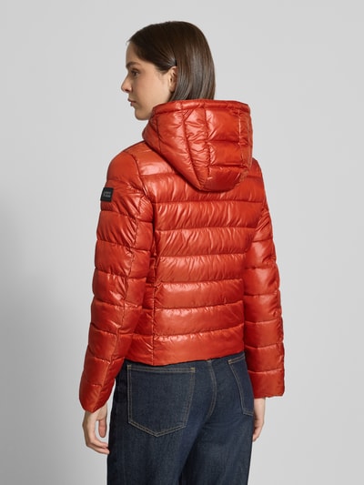 Frauenmodel trägt Regular Fit Jacke in Stepp-Optik von NAUTGÅRD in glänzendem Orange, glatte Oberfläche, Rückenansicht, Ganzkörperansicht. Rückenlänge, Schulterbreite, Brustweite und Ärmellänge in Größe S gegeben. Kapuze mit Stehkragen und Reißverschluss.