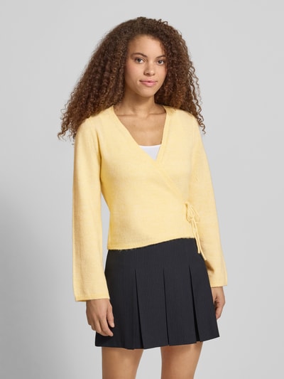 Frauenmodel trägt Regular Fit Strickjacke mit Woll-Anteil Modell 'COLO' von Only in Melange-Optik, Wickeloptik, Bindeband, V-Ausschnitt, Langarm, gerippte Abschlüsse, Strick Materialverarbeitung, Ganzkörperansicht von vorne.