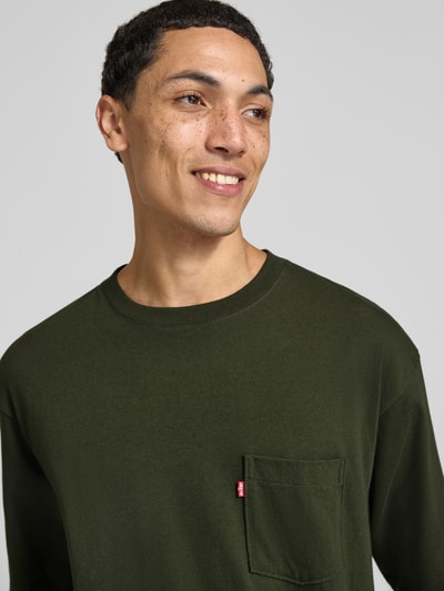 Męski model trägt Loose Fit T-Shirt aus reiner Baumwolle von Levi's® w kolorze ciemnozielonym, widoczna kieszonka, zbliżenie na górną część ciała