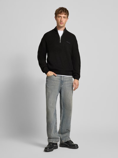 Männermodel trägt Regular Fit Troyer mit Reißverschluss von REVIEW in Schwarz mit Label-Stitching, Ganzkörperansicht von vorne.