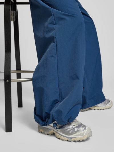 Frauenmodel trägt Nylon-Ballonhose im 90s-Stil - curated by Tinvcb in Dunkelblau, relaxed Fit, elastischer Bund, Detailaufnahme Beine.