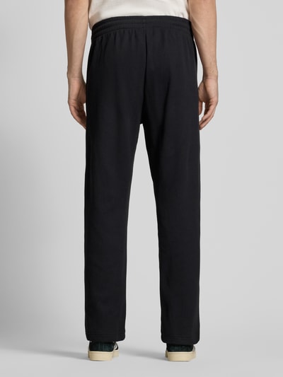 Männermodel trägt Straight Fit Sweatpants mit elastischem Bund Modell 'Essentials' von adidas Originals in Schwarz mit Strukturmuster, Ganzkörperansicht Rückansicht.