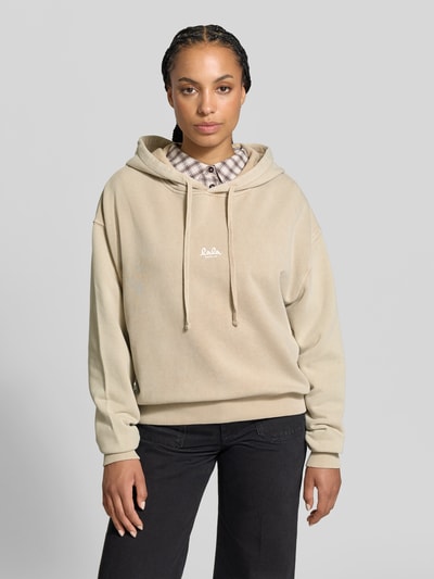Frauenmodel trägt Oversized Hoodie aus reiner Baumwolle von Lala Berlin in Beige mit Kapuze, Tunnelzug und Label-Print, Nahaufnahme Oberkörper.