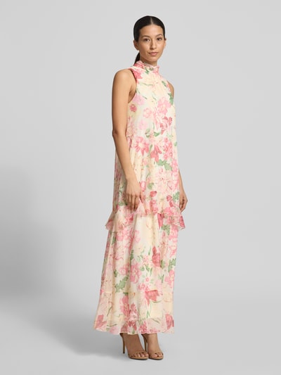 Vrouwenmodel draagt fließendes maxi-jurk met ruchedetail model 'SANNA' van Vero Moda, all-over bloemenmotief, chiffon, hooggesloten, mouwloos, maxilengte, volantzoom, onderjurk, detailopname zijkant.