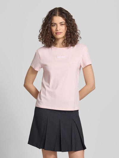 Frauenmodel trägt T-Shirt mit Rundhalsausschnitt und Logo-Stitching von Review aus Baumwoll-Mix mit Stretch-Anteil, Körpernaher-Schnitt, Rundhalsausschnitt, Rückenlänge bei Größe S: 53 cm, zartrosafarbene, glatte Struktur, Ganzkörperansicht von vorne.