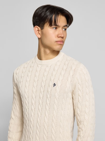 Männermodel trägt Strickpullover mit Zopfmuster und Logo-Stitching von REVIEW aus Baumwoll-Mix in Beige, Nahaufnahme Oberkörper.