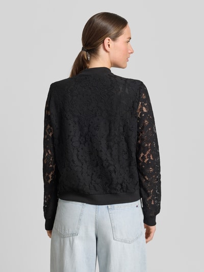 Frauenmodel trägt Regular Fit Blouson aus Baumwoll-Mix Modell 'HONEY' von Vero Moda, florales Allover-Muster, gehäkelte Materialverarbeitung, Farbe Schwarz, Ärmel Langarm, gerippter Rumpfabschluss, College-Kragen, Reißverschluss, Ganzkörperansicht Rückansicht.