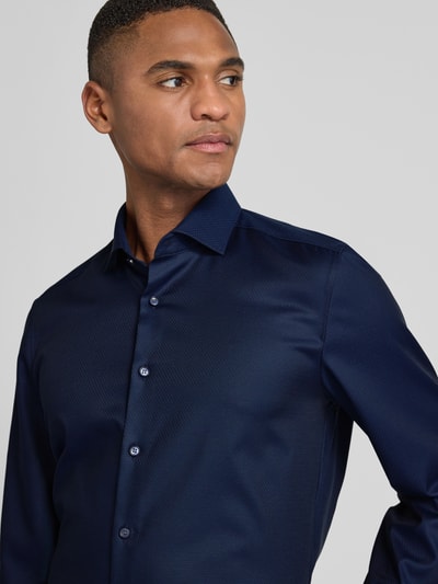 Männermodel trägt Slim Fit Businesshemd aus Baumwolle mit Kentkragen von OLYMP Level Five in Dunkelblau, Nahaufnahme Oberkörper. Baumwoll-Elasthan-Mix, Knopfleiste, elegante Textur.