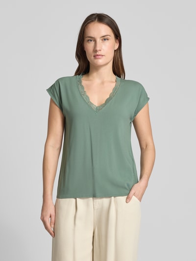 Modelka nosi Regular Fit T-Shirt mit Spitzenkragen Modell 'BELLA' od Vero Moda, gładka zieleń, krótki rękaw, jersey-stretch, krój regular fit, mieszanka wiskozy, widok całej sylwetki z przodu.