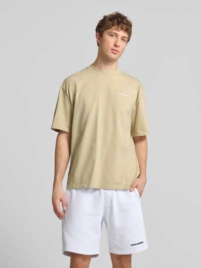 Männermodel trägt Oversized T-Shirt mit Logo-Stitching von Pegador in Beige, Reine Baumwolle, Oversized-Fit, Rundhalsausschnitt, Rückenlänge bei Größe M 73 cm, Herren T-Shirt, Ganzkörperansicht von vorne.