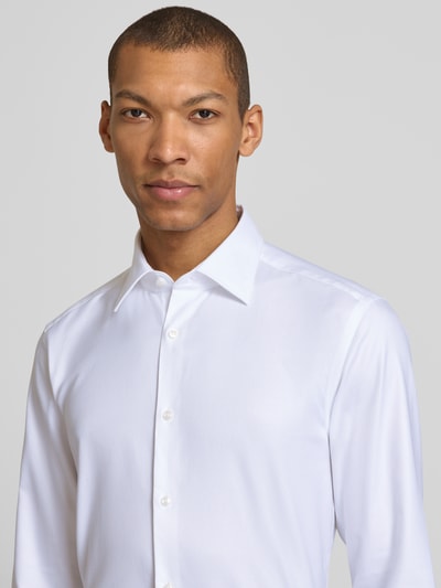 Männermodel trägt Slim Fit Businesshemd aus reiner Baumwolle Modell 'H-HANK-K' von BOSS in Weiß, Kentkragen, Nahaufnahme Oberkörper.