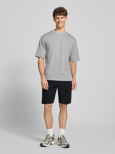 Męski model nosi Straight Fit Shorts mit Logo-Stitching Modell 'Fillip' od Blend, bawełna, strukturalny wzór, szorty z kieszeniami, elastyczny pas ze sznurkiem, szerokość w rozmiarze M: 39 cm, długość wewnętrzna nogawki: 26 cm, widok całej sylwetki z przodu.