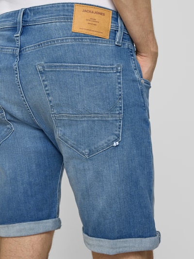 Mężczyzna nosi Jeansshorts mit Umschlag Modell 'RICK' von Jack & Jones, bawełniany materiał ze stretchem, krój regular fit, niebieski, szerokość w rozmiarze M: 42 cm, długość nogawki wewnętrznej w rozmiarze M: 23 cm, widok całej sylwetki z tyłu.