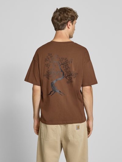 Männermodel trägt Relaxed Fit T-Shirt aus reiner Baumwolle Modell "DYLAN" von JACK & JONES in Braun mit Print-Detail, Ganzkörperansicht Rückansicht.