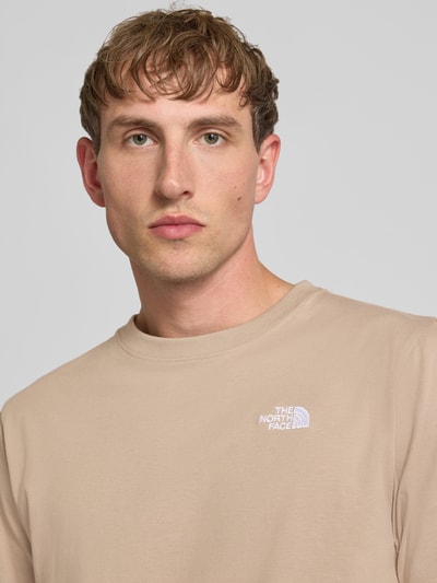 Männermodel trägt T-Shirt mit Label-Stitching und Rundhalsausschnitt von The North Face aus Baumwoll-Mix in Beige, Regular-Fit, Nahaufnahme Oberkörper. Herren T-Shirt, Rückenlänge bei Größe M: 72 cm.