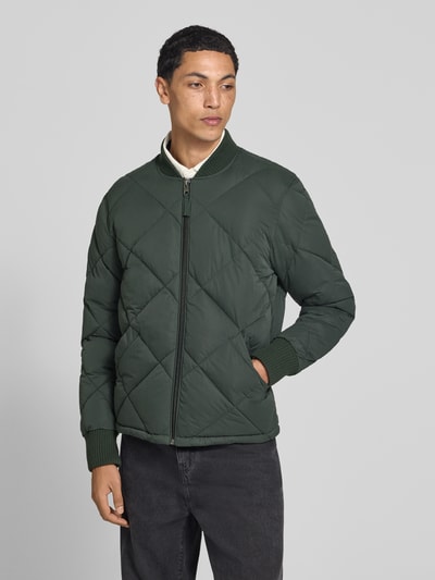 Männermodel trägt Regular Fit Steppjacke mit Stehkragen van Superdry in groene Stiksels look, steekzakken, ritssluiting, elastische mouwboordjes, ruglengte maat M 69 cm, schouderbreedte 46 cm, borstwijdte 58 cm, mouwlengte 59 cm. Ganzkörperansicht van voren.