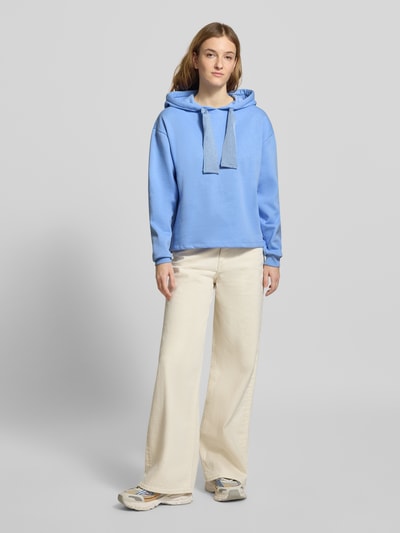 Modelka nosi Regular Fit Hoodie aus Baumwoll-Mix Modell 'CHILLI' od Pieces, niebieski, długi rękaw, gładki, kaptur ze sznurkiem, bluza sweat, krój regular fit, metka z logo, widok całej sylwetki z przodu.