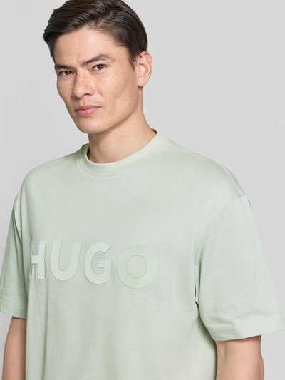 Männermodel trägt Relaxed Fit T-Shirt aus reiner Baumwolle Modell 'DINKEE' von HUGO, Optik: Unifarben, 3D Label-Print, Rundhals, Kurzarm, Materialverarbeitung: Jersey, Ganzkörperansicht von vorne.