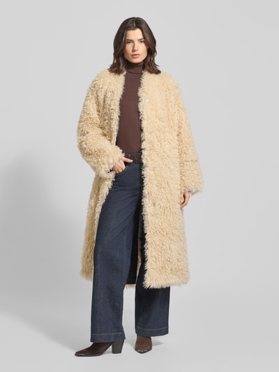 Frauenmodel trägt Mantel aus Kunstfell Modell 'Carolina' von STAND STUDIO in Beige, lockerer Schnitt, V-Ausschnitt, Ganzkörperansicht von vorne.