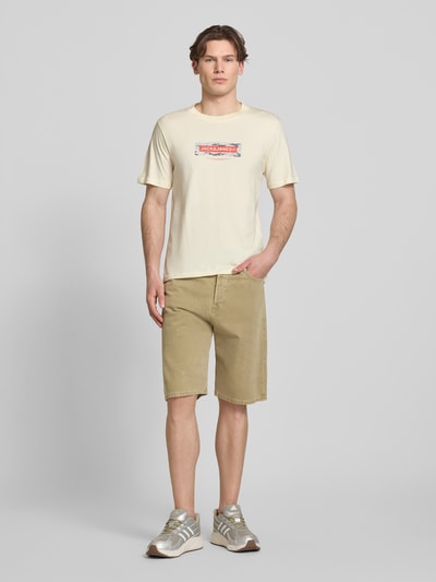 Männermodel trägt T-Shirt mit Logo und Rundhalsausschnitt von Jack & Jones in Beige, reine Baumwolle, Regular Fit, Ganzkörperansicht von vorne.