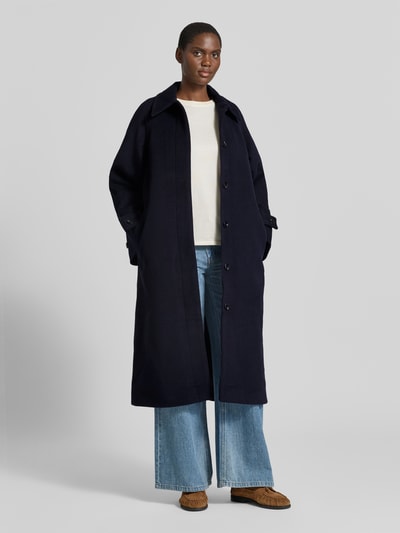 Frauenmodel trägt Mantel mit Ärmelriegeln Modell 'ALMA' von Samsøe Samsøe, dunkelblau, Regular Fit, Umlegekragen, verdeckte Knopfleiste, glatte Struktur, Ganzkörperansicht von vorne.