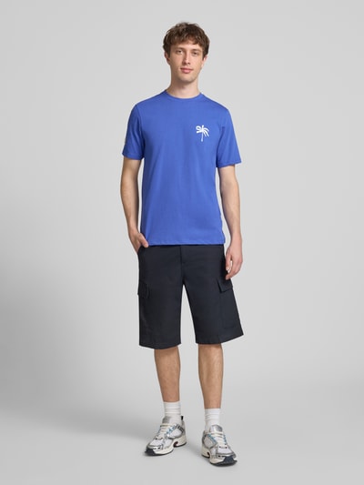 Männermodel trägt Herren T-Shirt mit Motiv-Print Modell 'SUN PALMS' von Blend in Blau, Reine Baumwolle, Regular-Fit, Rundhalsausschnitt, Rückenlänge 73 cm in Größe M, Ganzkörperansicht von vorne.